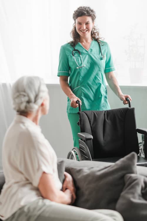 aide soignante avec un fauteuil roulant discute avec une personnée âgée dans une maison de retraite
